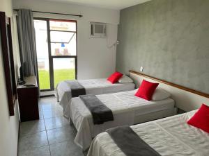 a hotel room with three beds with red pillows at Rasa Hotel in Búzios