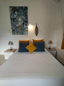 a bedroom with a white bed with blue and yellow pillows at Résidence Le Jardin des 4 Épices in Saint-Louis