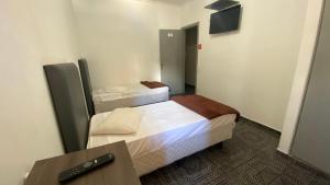 two beds in a room with a remote control at Hotel dos Nobres in Poços de Caldas