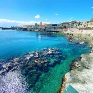 a view of a beach with blue water and buildings at Casa Maria in Siracusa