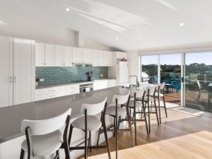 eine Küche mit weißen Schränken und eine Bar mit Hockern in der Unterkunft Coastal Luxury in Rye