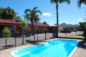 a swimming pool in front of a house with palm trees at Cunningham Shore Motel in Lakes Entrance