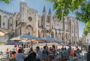 un groupe de personnes assises à des tables devant un château dans l'établissement Ô portes du Palais, à Avignon