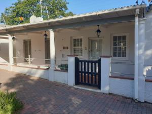 une maison blanche avec un portail et une terrasse couverte dans l'établissement Wishford Cottage on Worcester, à Grahamstown