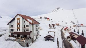 un bâtiment dans la neige avec une montagne en arrière-plan dans l'établissement Cabana Parang, à Rânca