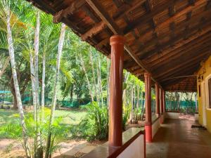 a porch of a house with red columns and palm trees at Paradise Vana Vilasa Homestay with Swimming pool in Auroville