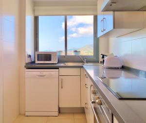 a white kitchen with a microwave and a window at Cofradia Penthouse in Alcudia