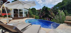una piscina con sillas y una sombrilla junto a una casa en Casa Maria Comprida Araras, serviço incluído, 5 quartos, piscina e área gourmet en Petrópolis