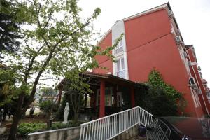 a red building with a white porch next to a tree at Hotel Matal in Međugorje