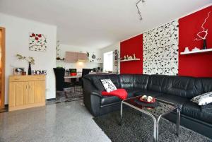 ein Wohnzimmer mit einem schwarzen Ledersofa und einer roten Wand in der Unterkunft Apartment Bergen auf Rugen 1 in Mölln-Medow