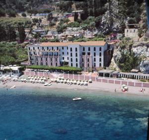 een groot gebouw op een strand met parasols in het water bij Hotel Lido Mediterranee in Taormina