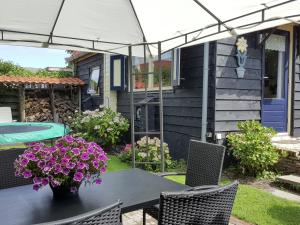 eine Terrasse mit einem Tisch mit lila Blumen und einem Sonnenschirm in der Unterkunft Holiday Home in t Zand close to the Dutch coast in 't Zand