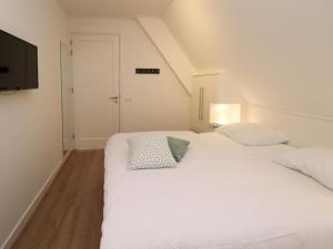 1 dormitorio con 1 cama blanca y TV en Thatched villa with lounge set, right at the water, en Delfstrahuizen