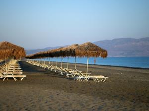 a row of straw umbrellas and chairs on a beach at Caldera Creta Paradise in Plataniás
