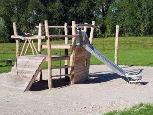 a wooden playground with a slide in a park at Tidy chalet with a microwave, near the Wadden Sea in Tzummarum
