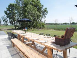 a long wooden table with chairs and an umbrella at Elegant Farmhouse in Zuidzande with Private Garden in Zuidzande