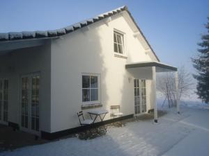 Casa blanca con mesa y 2 sillas en la nieve en Cosy holiday home overlooking the meadows, en Spijk