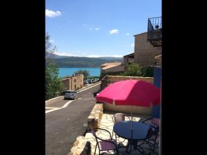 a table and chairs with a pink umbrella on a balcony at Perle rare in Sainte-Croix-de-Verdon