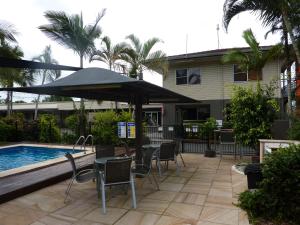 eine Terrasse mit einem Tisch und einem Sonnenschirm neben einem Pool in der Unterkunft Country Plaza Motor Inn in Mackay
