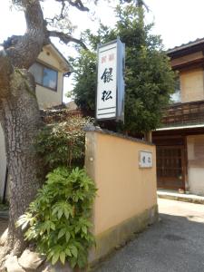 un cartel en una pared junto a un árbol en Minshuku Ginmatsu en Kanazawa