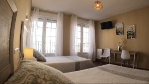 1 dormitorio con 2 camas, escritorio y 2 ventanas en Hostal Santiago en Carrión de los Condes