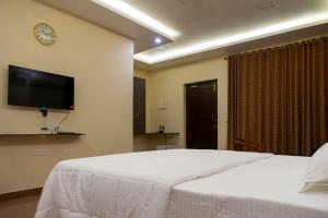 a bedroom with a white bed and a tv on the wall at Pranaav Beach Resort in Puducherry
