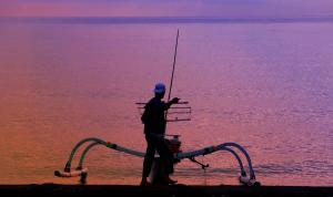 a man holding a fishing rod on the end of a boat at Santai Hotel in Amed