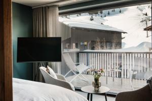 a room with a bed and a balcony with a television at Berghotel Biberkopf in Warth am Arlberg