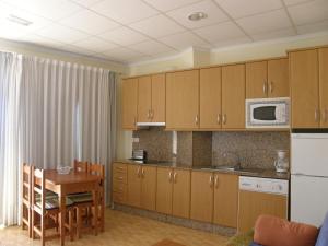 cocina con armarios de madera, mesa y microondas en Apartamentos Bellavista, en Puerto de Mazarrón