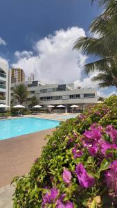 a swimming pool with purple flowers in front of a building at Ponta Negra Beach Flat Prime in Natal