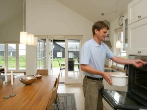 a man standing in a kitchen putting a pot in the oven at 8 person holiday home in Nysted in Nysted