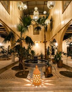 un vestíbulo con mesa, palmeras y lámparas de araña en Kasbah Mohayut, en Merzouga