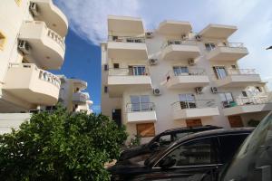 wysoki biały budynek z samochodami zaparkowanymi przed nim w obiekcie Hotel Four Islands w mieście Ksamil