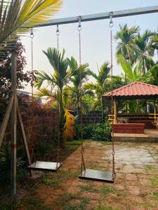 a swing in a yard with a bench and palm trees at Oasis Resort in Diveagar