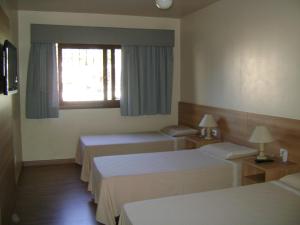 a hotel room with three beds and a window at Hotel Areias Brancas in Rosário do Sul