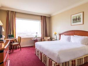 a hotel room with a bed and a desk and a window at Pullman Bucharest World Trade Center in Bucharest