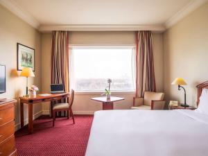 a hotel room with a bed and a desk and a window at Pullman Bucharest World Trade Center in Bucharest