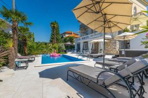 a pool with chairs and an umbrella next to a house at Villa Vita Apartments in Crikvenica