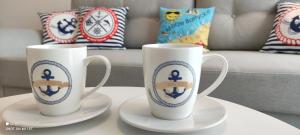 dwa białe kubki kawy siedzące na talerzach na stole w obiekcie Apartament Morski - Olimpijska 2, Mielno w mieście Mielno
