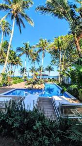 uma piscina de resort com palmeiras e uma praia em Brisa do Mar Barê Praia Hotel - Praia de BAREQUEÇABA em São Sebastião