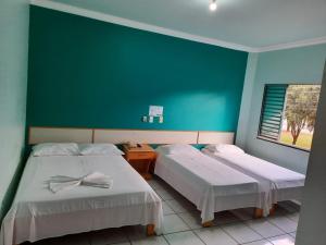 two beds in a room with a green wall at Bravo City Hotel Nova Mutum in Nova Mutum