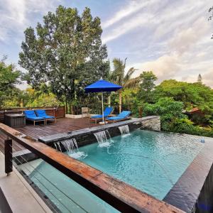 una piscina con cascada, sillas azules y sombrilla en St Lucia Hilltop Guest House en St Lucia