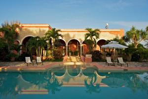 a house with a swimming pool with chairs and an umbrella at Hacienda Sacnicte in Izamal