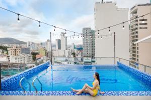 una mujer sentada en el borde de una piscina en un edificio en Ale Nha Trang Hotel, en Nha Trang