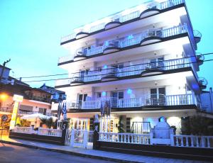 a large white building with balconies on a street at Hotel San Antonio in Paralia Katerinis