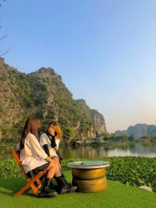 two women sitting on a chair next to a lake at Trang An Memory Homestay in Ninh Binh