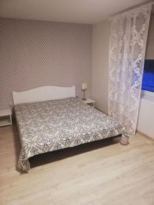 a bedroom with a bed with a bedspread and a curtain at Vėjo 16 in Biržai