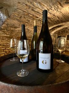 three bottles of wine sitting on a barrel with wine glasses at Chambre à la ferme in Précy-le-Sec