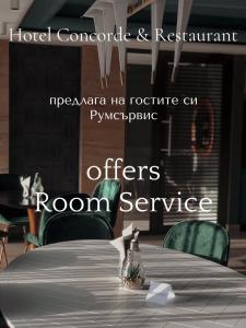 una habitación con una mesa con sillas verdes y un cartel que dice que ofrece servicio de habitaciones en Hotel Concorde, en Veliko Tŭrnovo
