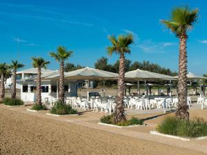 a row of palm trees and white tables and chairs at Apartment in Albarella near Sandy Beach in Isola Albarella